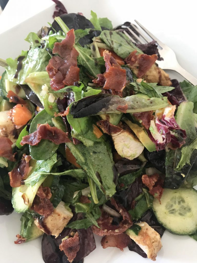 A salad with bacon and cucumber on top of it.
