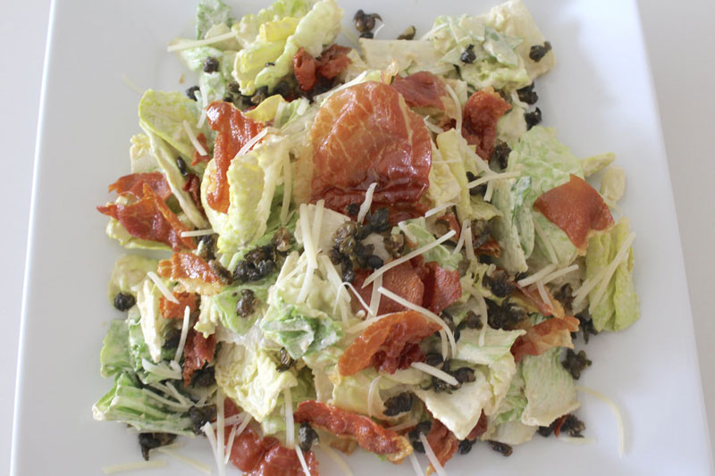 A salad with lettuce, tomatoes and olives on top.
