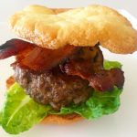 A hamburger with bacon and lettuce on top of a bun.