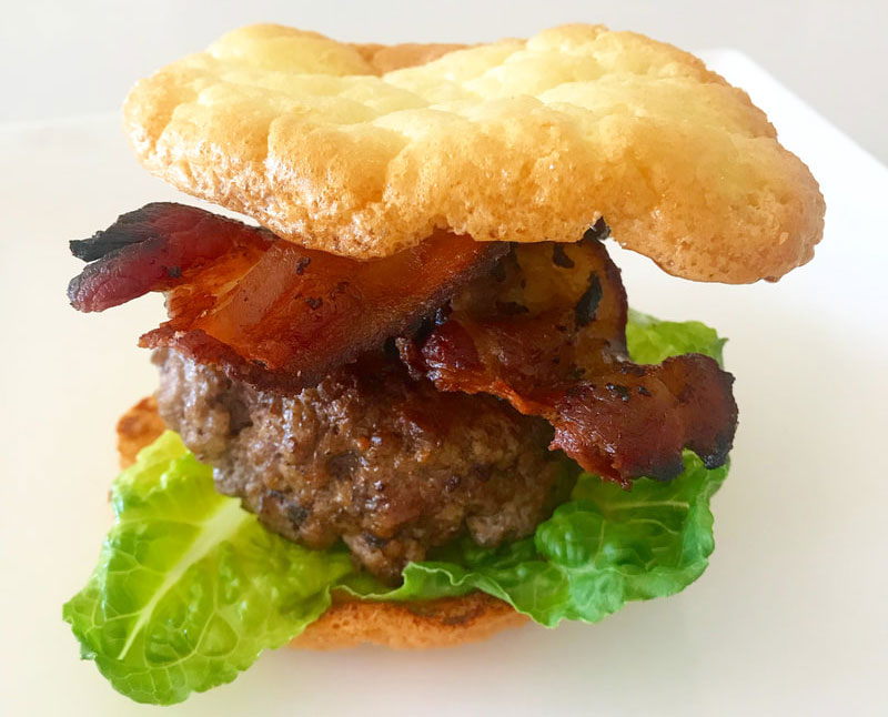 A hamburger with bacon and lettuce on top of a bun.