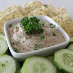 A bowl of dip with crackers and cucumbers